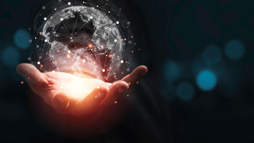 A glowing digital globe with interconnected network lines and nodes hovering above an open hand, symbolizing global connectivity, data networks, and advanced technology on a dark background.